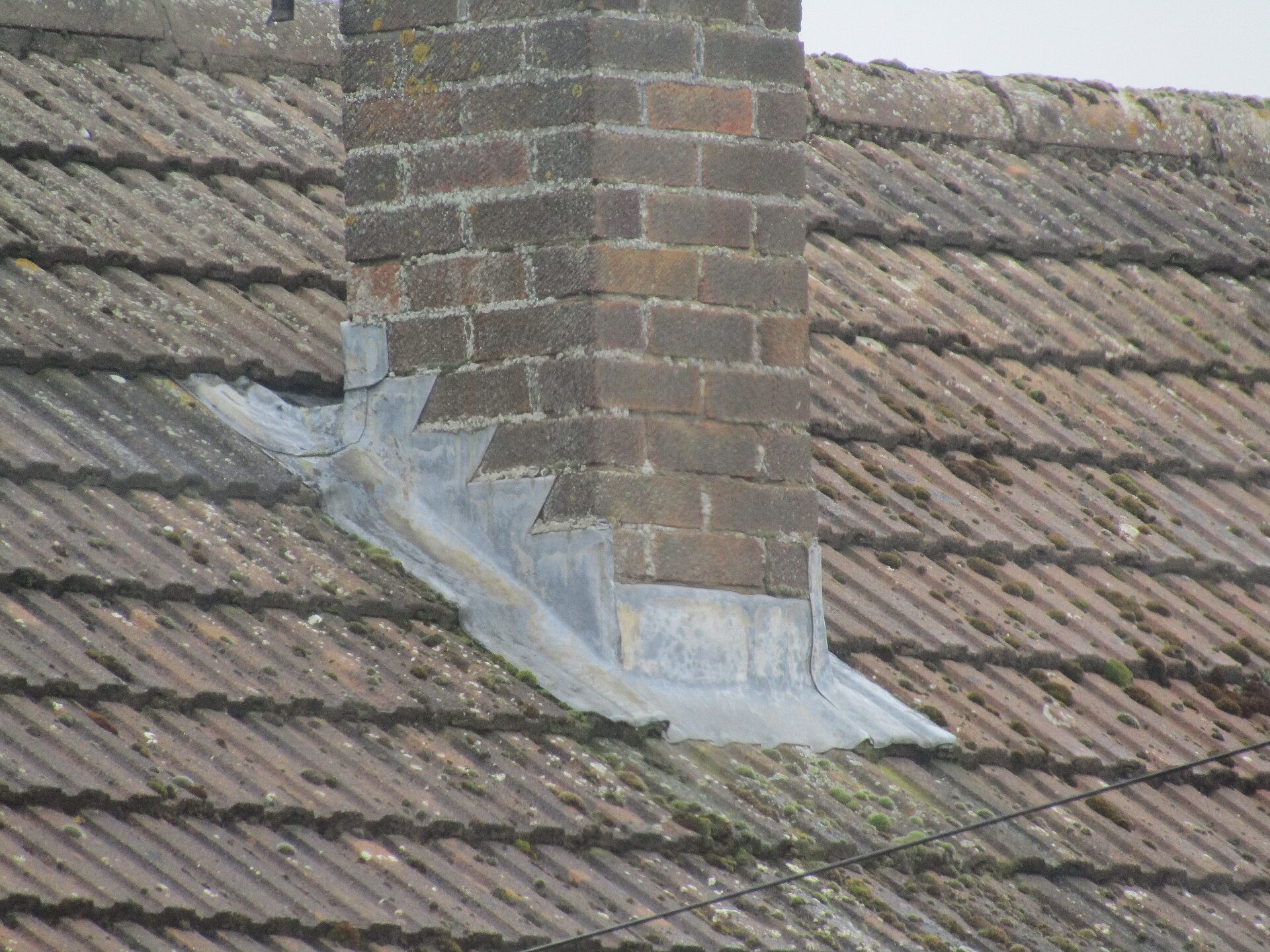 Lead flashing wrapped around the base of a brick chimney on a tiled roof