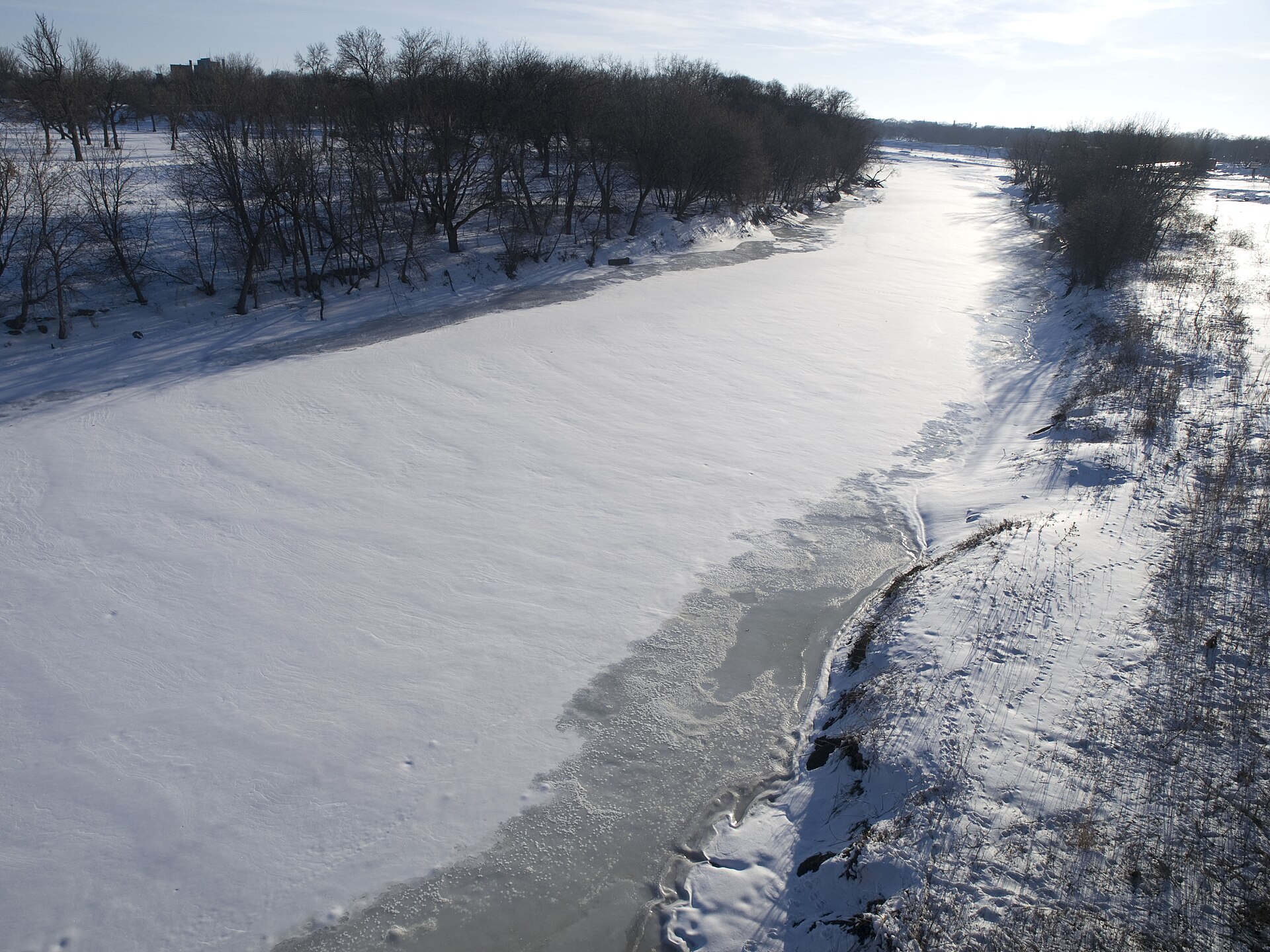 The frozen Red River of the North under snow, with bare trees along its banks